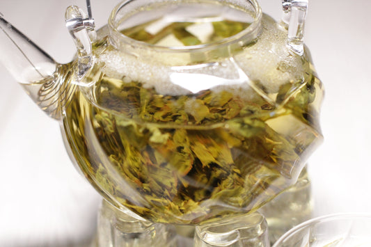 Glass teapot with loose leaf oolong tea steeping, showing golden infusion and unfurling leaves