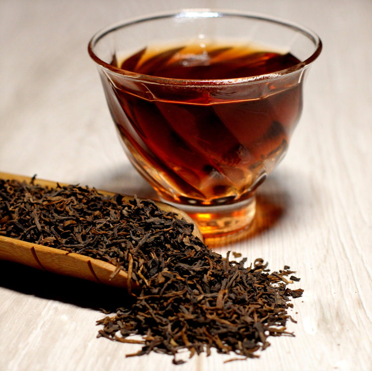 Amber black tea in a glass cup with loose leaf tea beside it