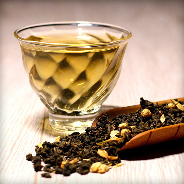 Glass cup of oolong tea with golden infusion and loose tea leaves on a wooden surface
