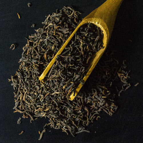 Loose leaf tea with dried leaves and a wooden scoop on a dark surface